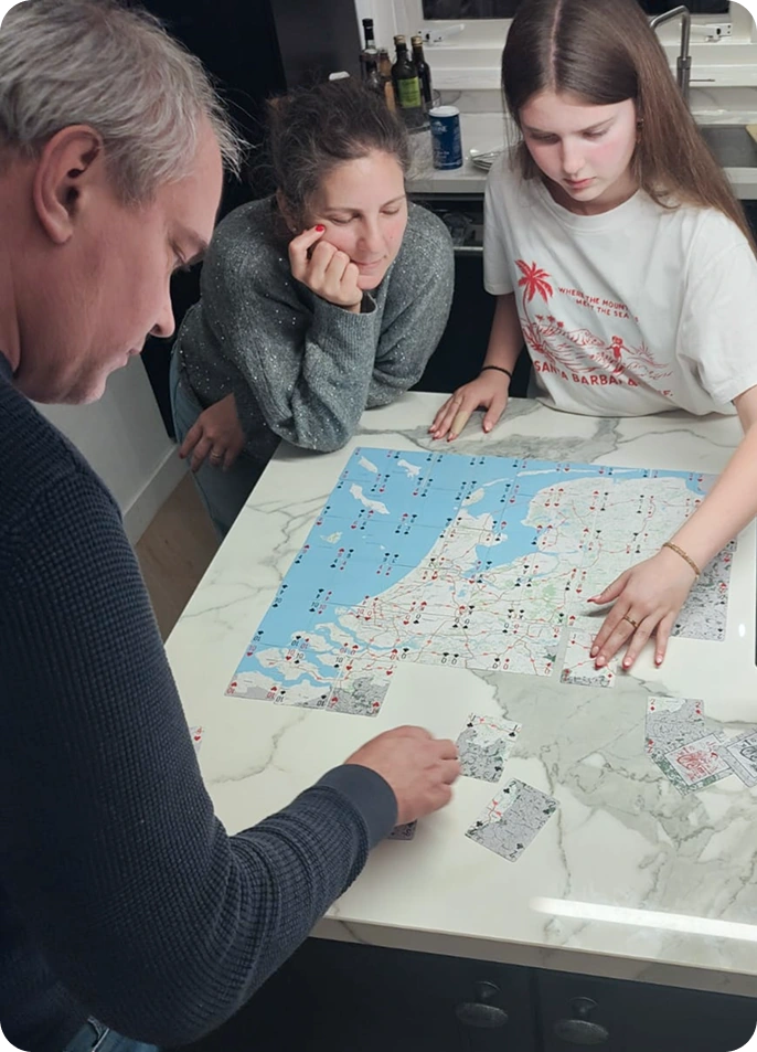 Three people working together on the map puzzle spread across a table