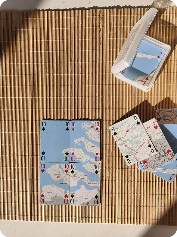 An open Shuffle Puzzle case and map playing cards in sunlight on a woven mat